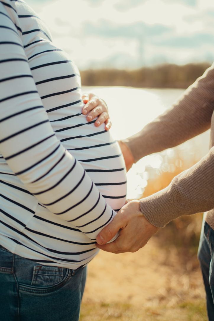 Werdende Eltern halten gemeinsam liebevoll den Babybauch im Gegenlicht
