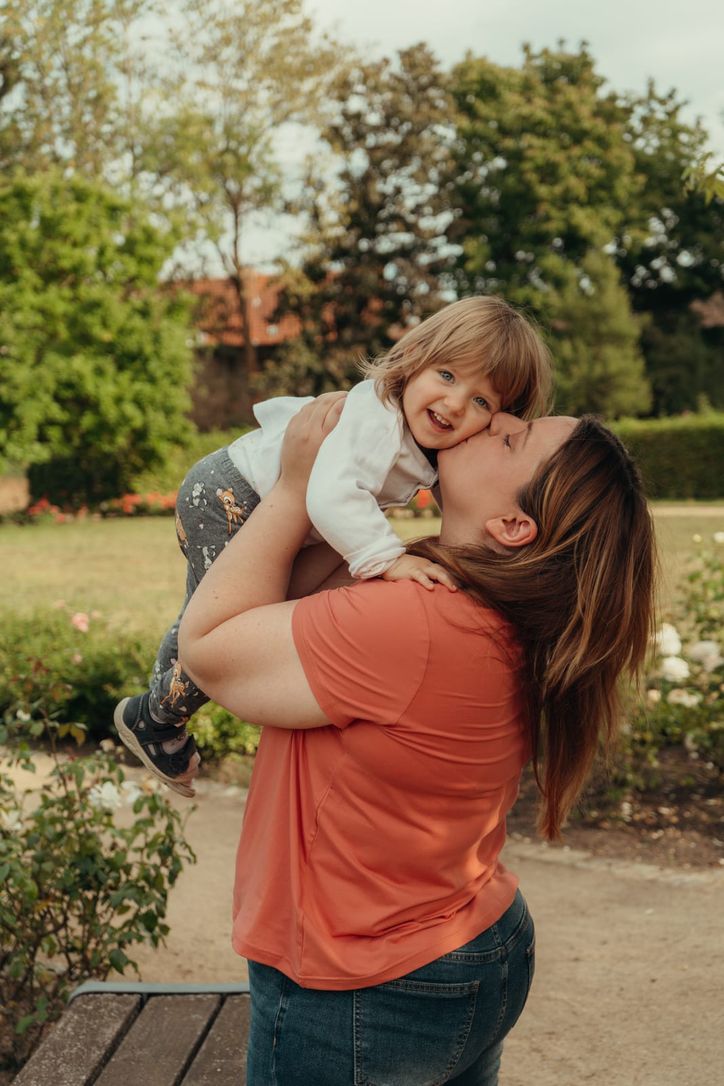 Mutter küsst ihr lachendes Kleinkind im Garten