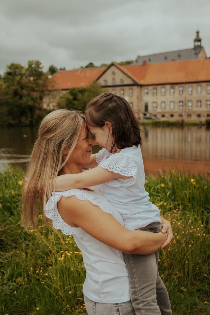 Mutter und Tochter umarmen sich Stirn an Stirn vor historischer Kulisse am Fluss