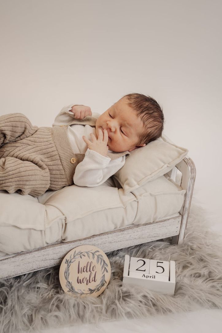 Neugeborenes schläft auf Mini-Sofa neben Holzschild „hello world" und Datumsblöcken