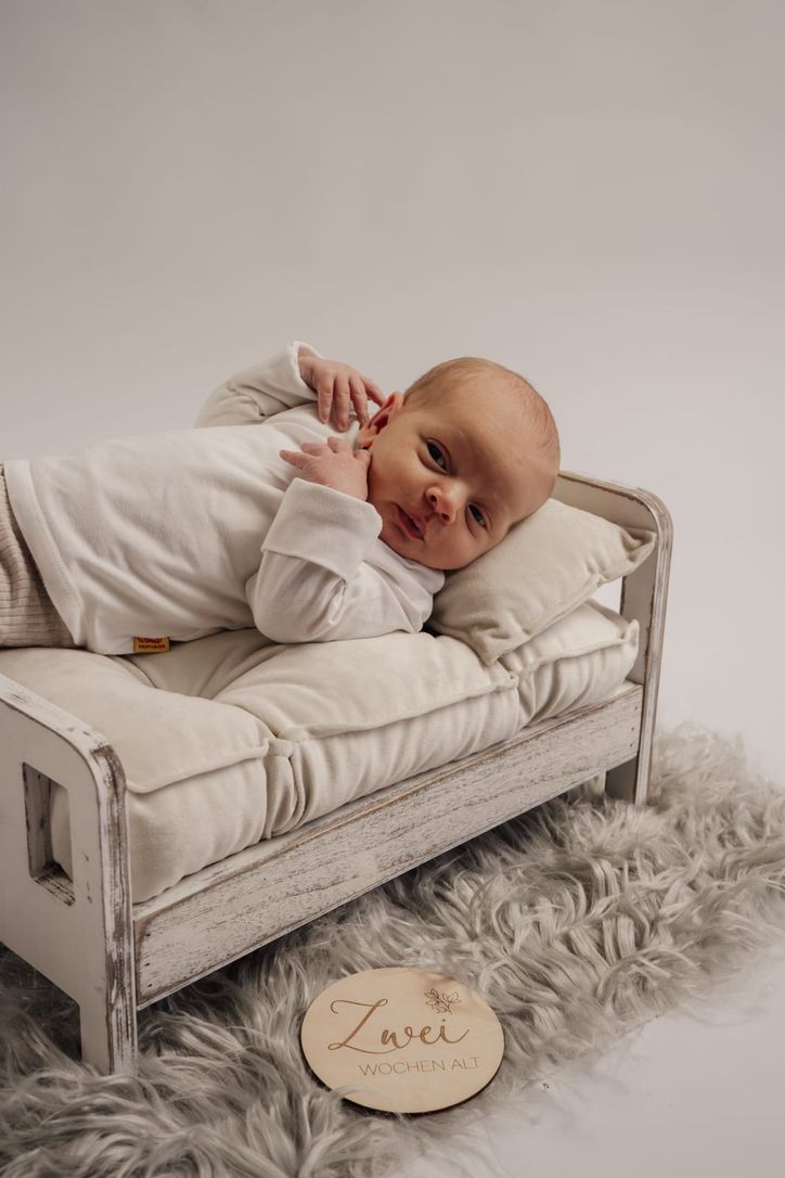 Neugeborenes auf Mini-Sofa neben Holzschild „Zwei Wochen alt"