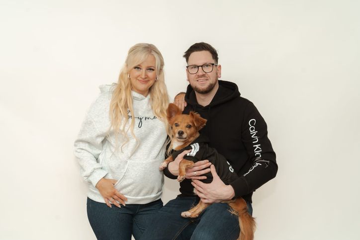 Werdende Eltern mit ihrem Hund lächeln im Fotostudio in die Kamera