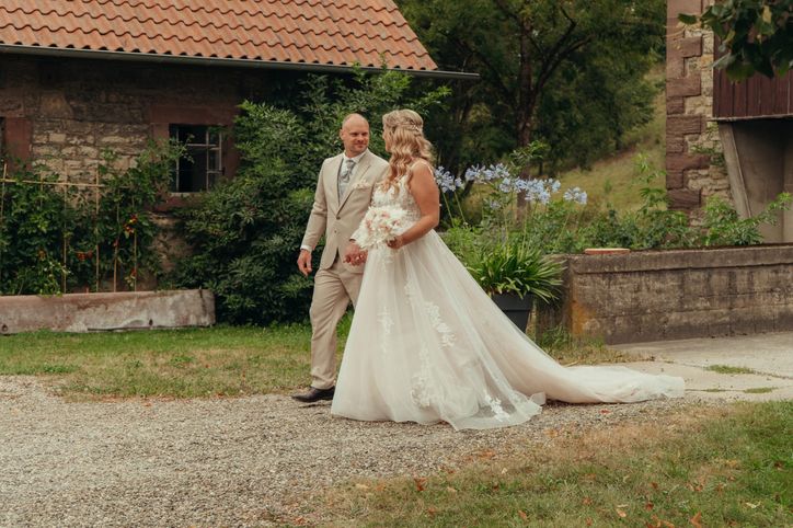 Brautpaar spaziert Hand in Hand an einem alten Gutshof vorbei