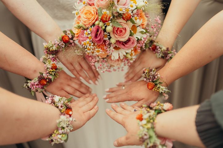 Hände der Brautjungfern mit Blumenarmbändern um den bunten Brautstrauß