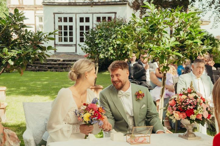 Brautpaar hält lächelnd den bunten Brautstrauß bei der Trauung im Garten