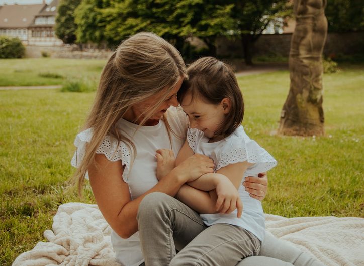 Mutter und Tochter kuscheln lachend auf einer Picknickdecke im Park